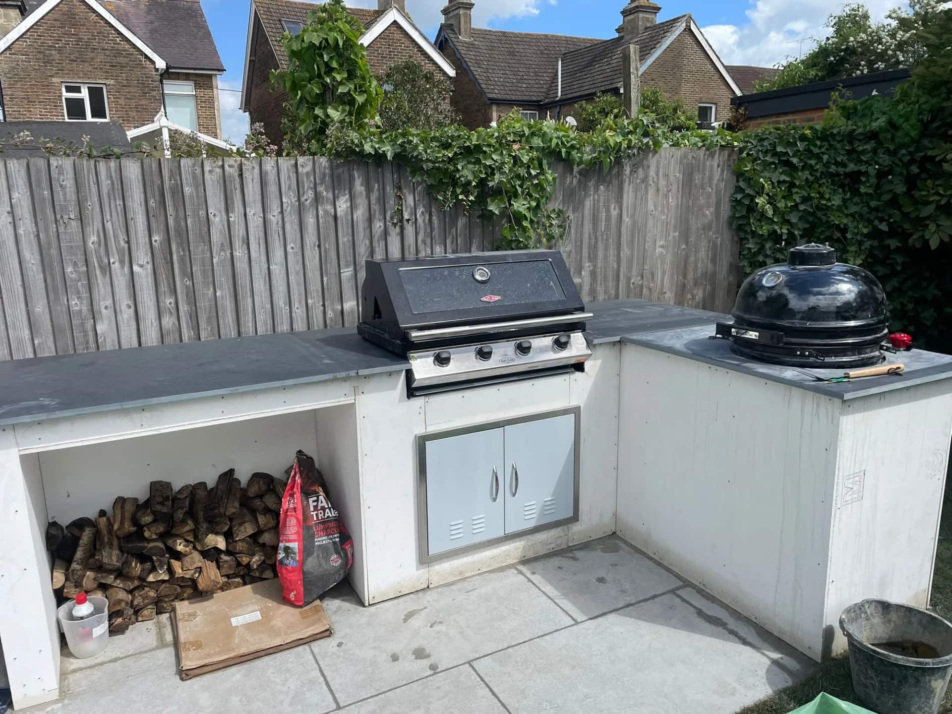 Outdoor kitchen with a built-in gas grill, kamado barbecue, zinc worktops and a log store