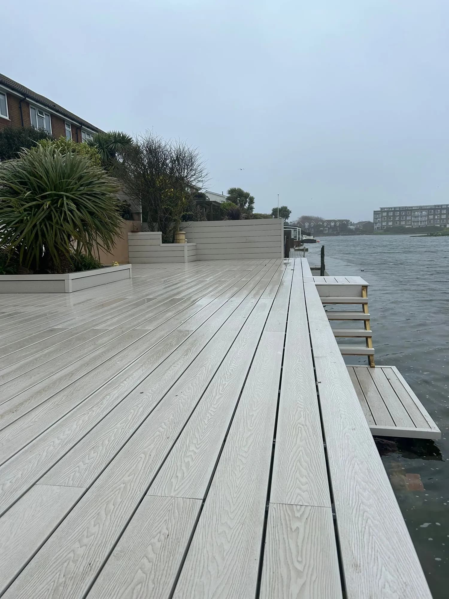 Grey composite decking running along an estuary edge with a slatted privacy screen and planters